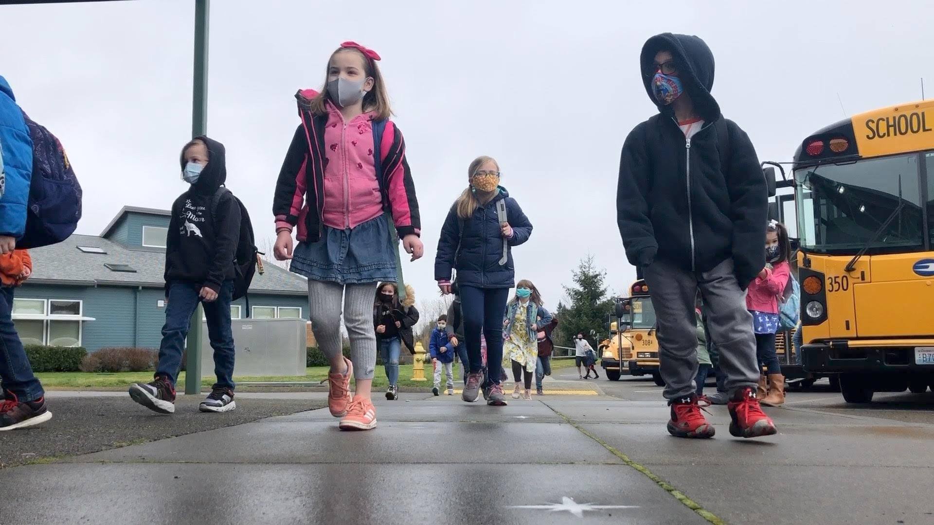 Elementary students walking away from a bus, wearing COVID-19 masks.