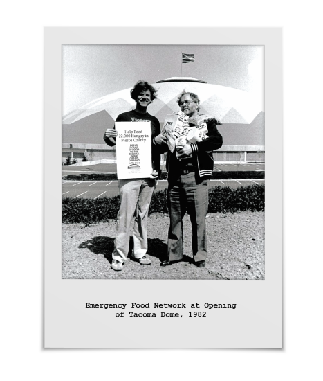 Two men stand in front of the newly opening Tacoma Dome, representing the Emergency Food Network, 1982