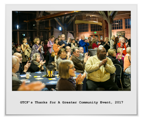 Lots of people, standing and sitting, applaud for the shared work of building a thriving community in 2017 at the Foss Waterway Seaport Museum.